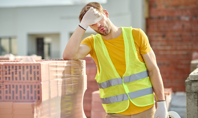 overworked male in a protective vest sighing while holding forehead